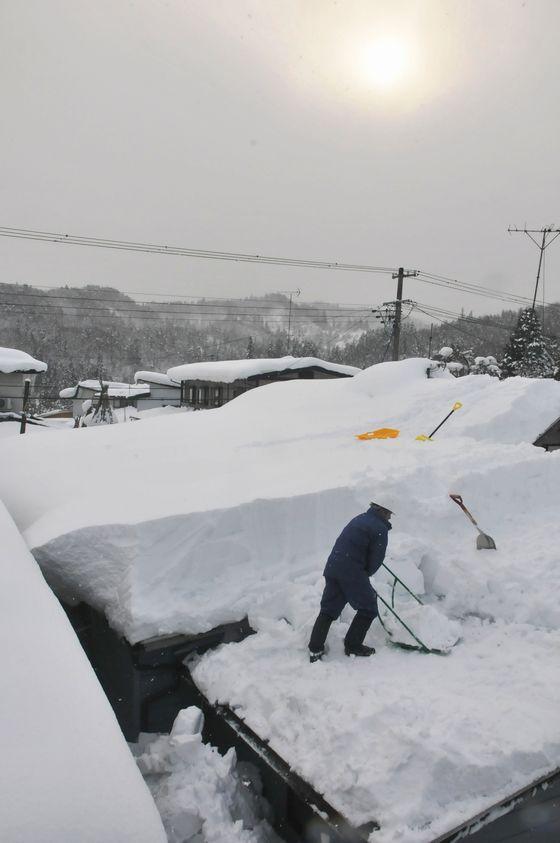 屋根の上の雪下ろしをしている人を写した写真