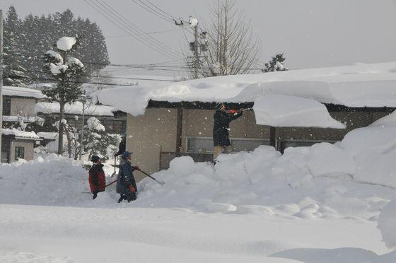 公民館の屋根にスコップを入れている雪下ろし作業の様子の写真