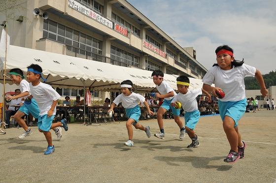 全校児童が参加するリレーでバトン代わりのかぼちゃを持ちゴールに向かって走る男女の生徒たちの写真
