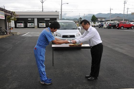 納車式で納入業者から町長に対し 鍵と車検証などが手渡されている様子の写真