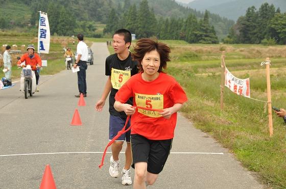 松程地内で選手たちが9区から10区のタスキリレーをしている写真