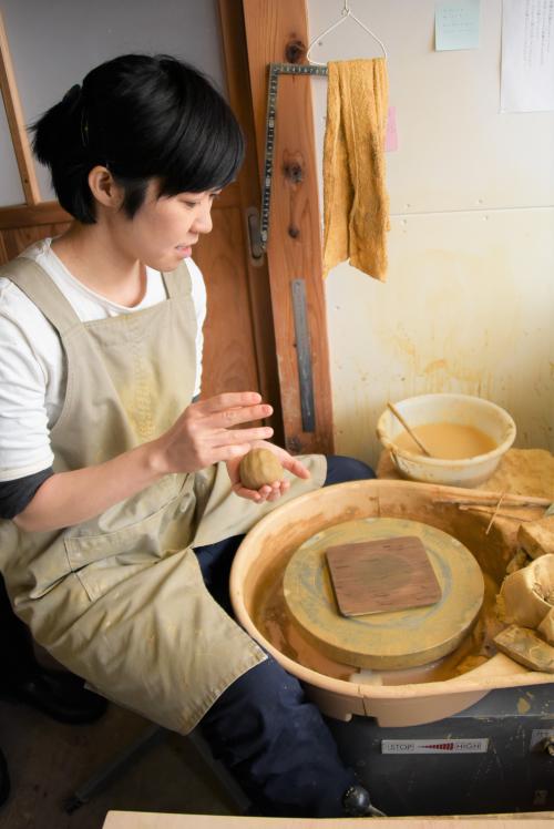粘土を手に、ろくろの前に座る長岡さん