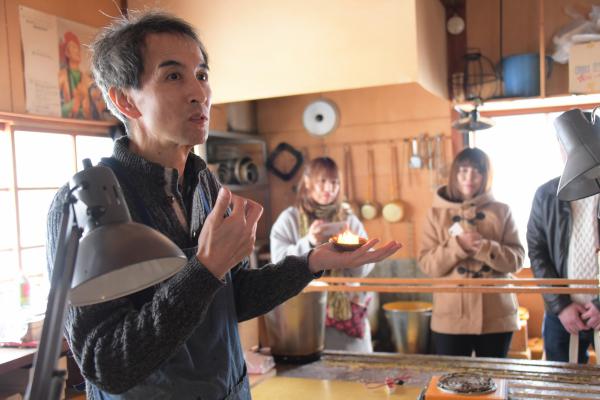 蜜ろうキャンドルを手に説明する安藤さんの写真