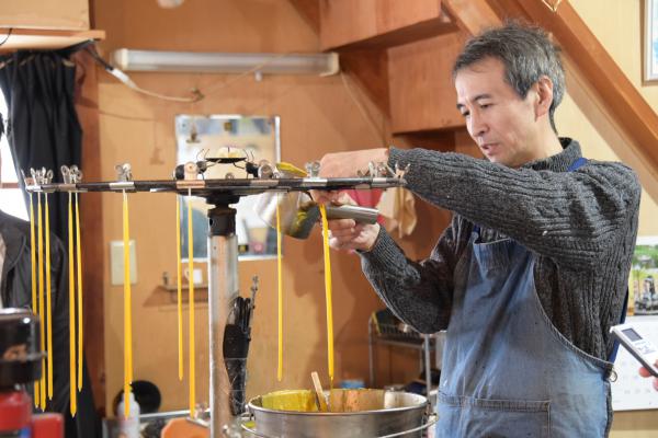 溶かした蜜ろうを鍋から掬い、芯にまわしかけてろうそくを作っている様子