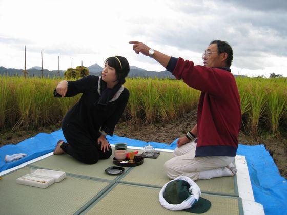 青いシートの上の畳に座っている遠くの山を指さす男性とその山を見つめる女性の写真