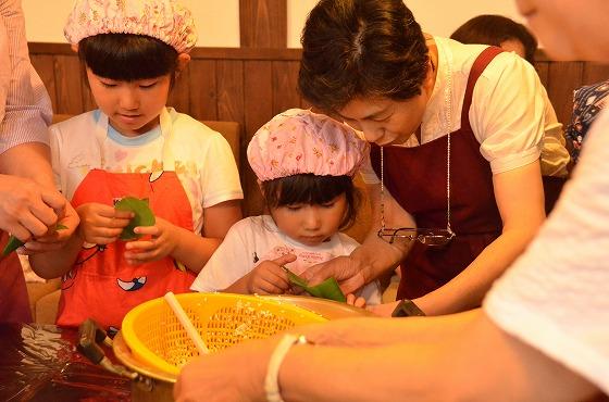 子どもたちが先生から教わりながら笹巻き作りをしている様子の写真