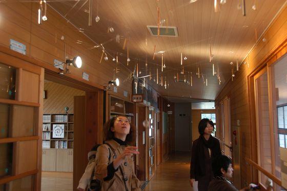 天井に吊るされたオブジェを引っ張り音を鳴らしている女性と来場客の男女の写真