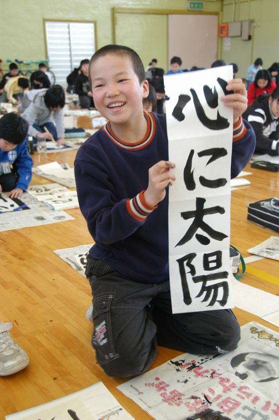 宮宿小書き初め大会で書いた「心に太陽」を持ってこちらに見せている児童の写真