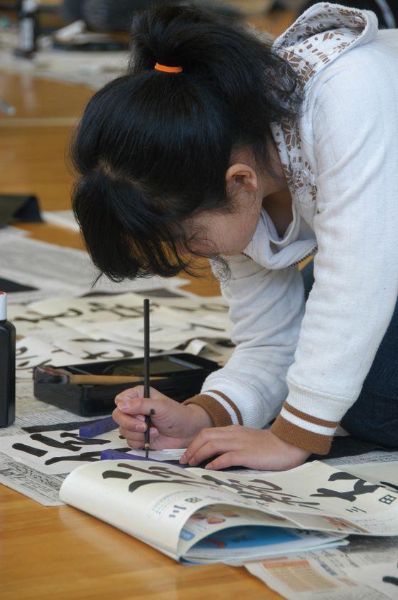 宮宿小書き初め大会で、最後の仕上げに小筆で名前を書いている児童の写真