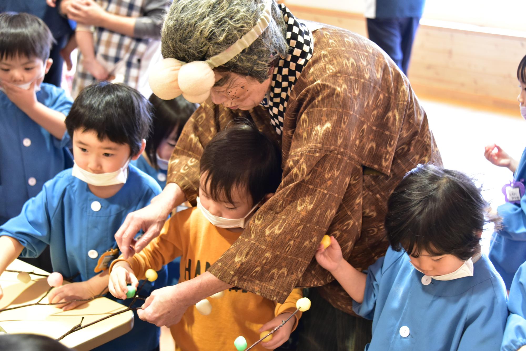 語りの会つむぎの皆さんと団子を下げる園児
