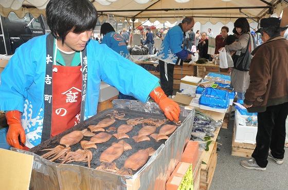 屋外のテントに出店した気仙沼市本吉町の海産物コーナーでイカを焼く様子の写真