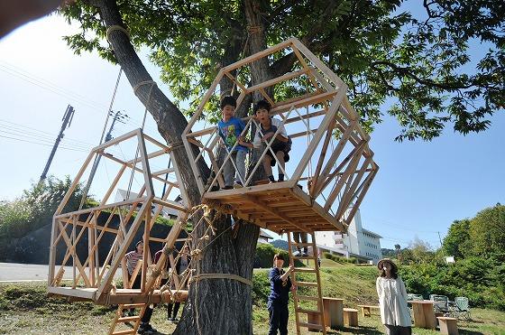 Asahi自然観敷地内にある栗の木に設置されたツリーハウスにいる2人の子どもとツリーハウスに登るためのはしごを持っている女性とツリーハウスを眺めている来訪者の写真1