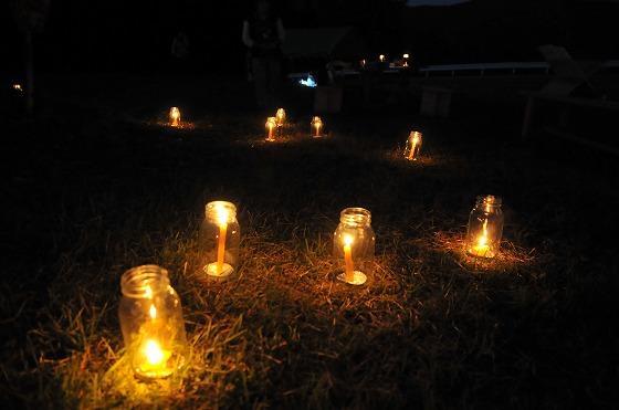 芝生の上に置かれている瓶や加工したペットボトルに入っている火を灯す9つのキャンドルの写真