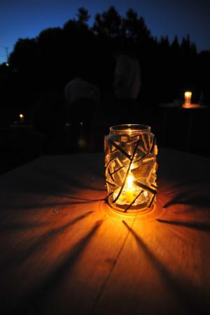 夜空を背景にデッキの上に置いてあるデザインが加えられた瓶に入っている火を灯すキャンドルの写真