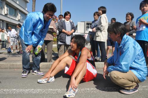 人に囲まれて完走して座り込んでいる選手の写真