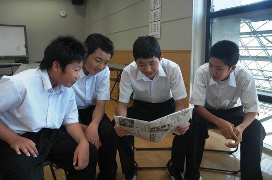 自分たちの記事が載った新聞を読む中学生の写真