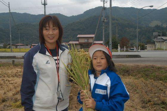 束ねた稲を両手で持っている女児児童と女性教師との2ショットの写真