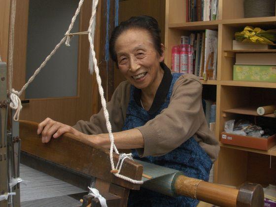 笑顔で機織りをする阿部知子さんの写真