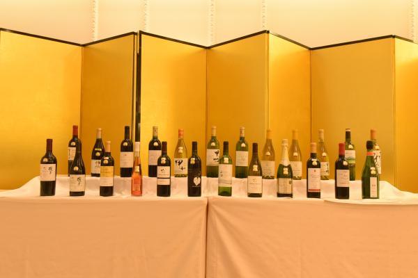 金色の屏風の前に並べられたコンクールで金賞を受賞した24銘柄のワインの写真