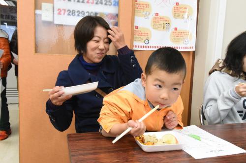学校給食メニューの試食会で美味しそうに食べている親子の写真