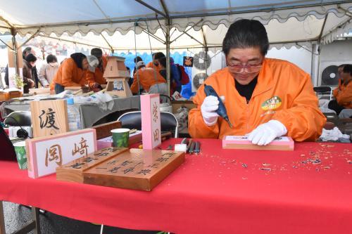 町建設総合組合のブースで表札彫りの実演をする様子の写真