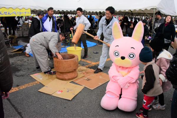 桃色ウサヒの横で餅つきをする様子の写真