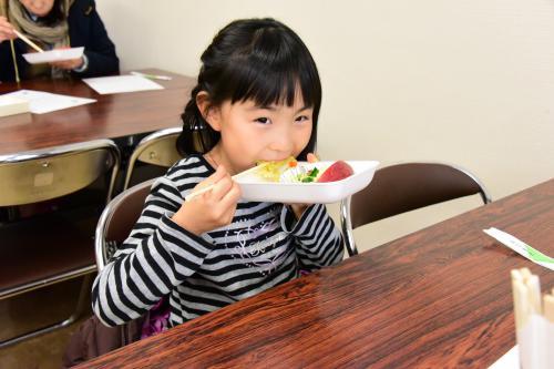 学校給食メニューの試食会で給食を食べて喜ぶ女の子の写真