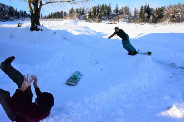 棚田の入り口付近で、ベニヤ板を貼り合わせて磨いた手づくりの「雪板」で雪遊びをしているかたが、転んでいる写真
