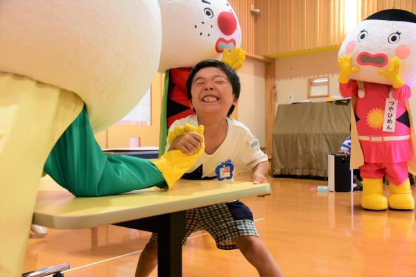 朝ごはんをしっかり食べてきている男の子がおこめんジャーグリーンと腕相撲で勝負する様子の写真