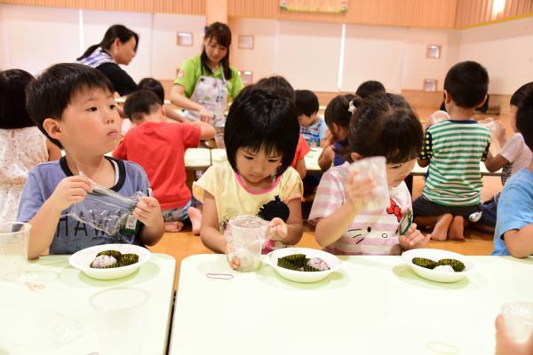 園児たちもご飯を入れたコップを振っておにぎり作りをしている様子の写真