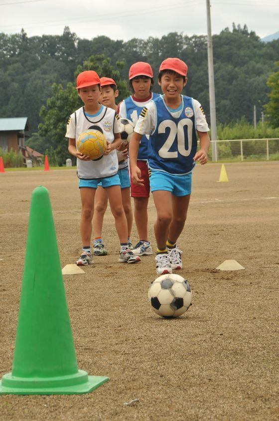 大谷小学校の校庭で蹴ったサッカーボールをカラーコーンに当てるゲームをしている児童たちの写真