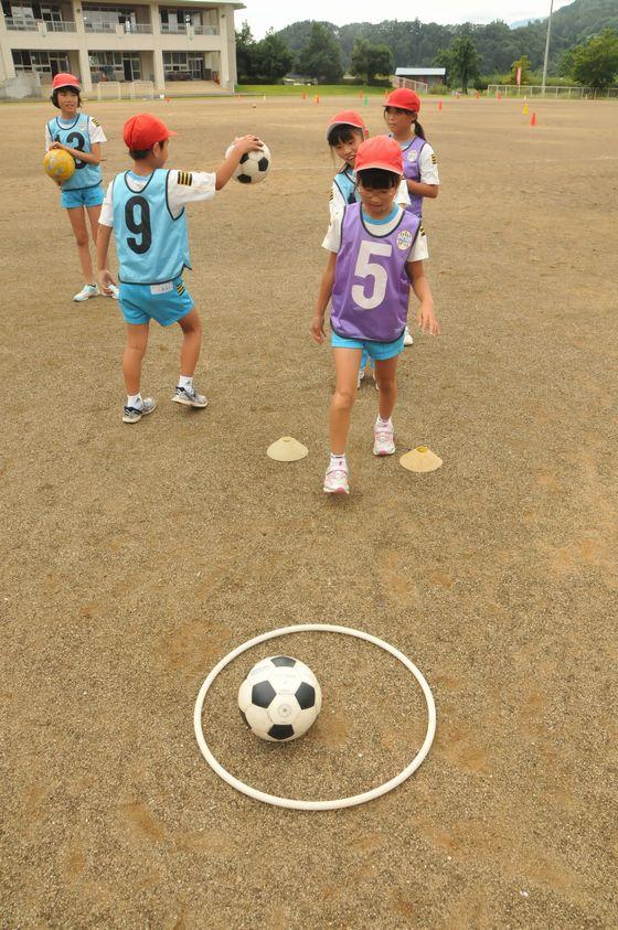 大谷小学校の校庭でボールを蹴って白い輪の中に入れるゲームをしている児童たちの写真
