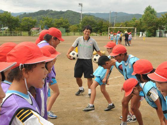 ミニゲーム終了後にあいさつを交わす児童たちと2つのサッカーボールを手に笑顔を見せるコーチの写真