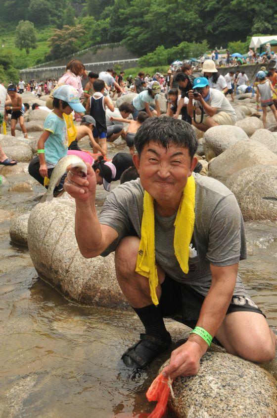 渓流祭りで川魚を掲げる男性参加者の写真