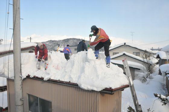 屋根に上がり雪をかき分ける雪下ろし作業の様子の写真