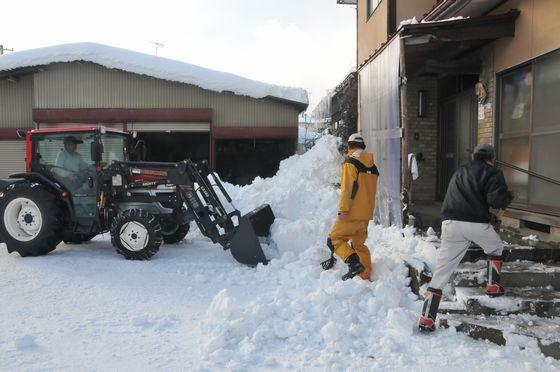 雪下ろし作業で地上にたまった雪を集めている様子の写真1