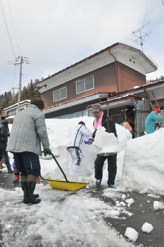 玄関の前に山積みになった雪を10人がかりで片付けている写真