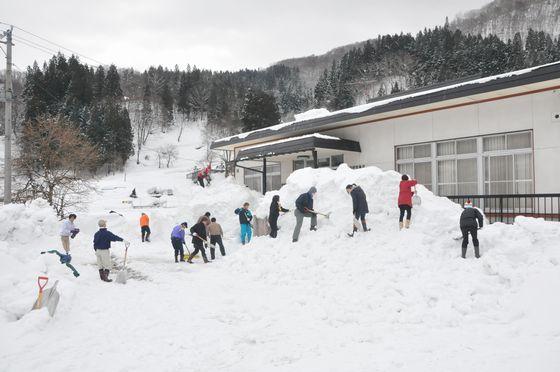 15人がかりで公民館入口付近の排雪作業を行っている様子の写真