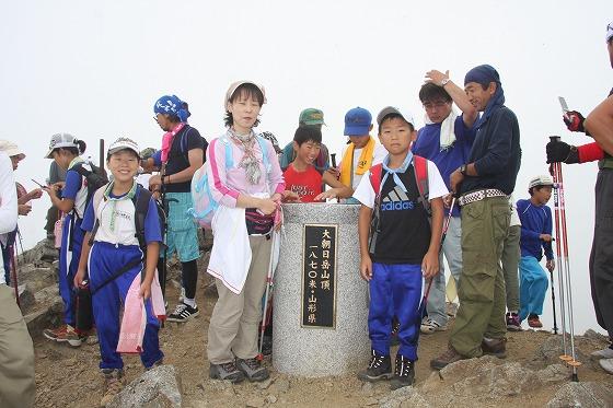 「大朝日岳山頂」と表記された石柱とともに写真撮影などを行っている様子の写真