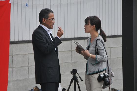 新聞記者から取材を受けている白田重明総務部長の写真