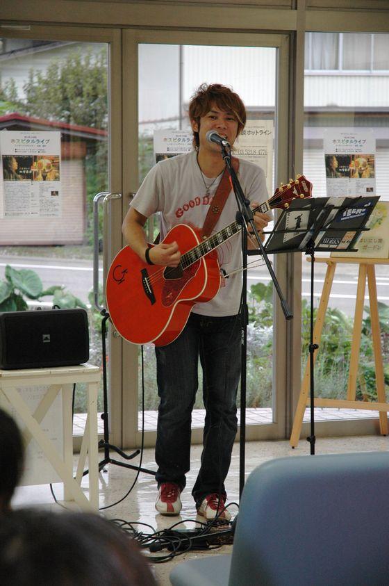 ギターの弾き語りで歌う松尾貴臣さんの写真