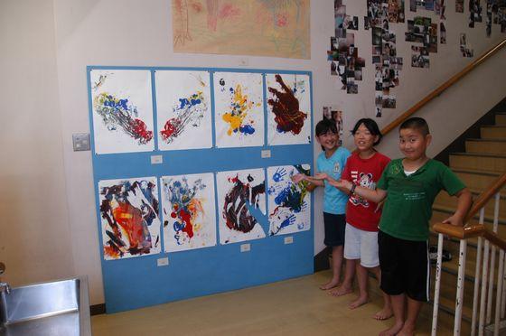 旧上郷小学校の階段の踊り場に展示している絵を紹介する3人の児童の写真