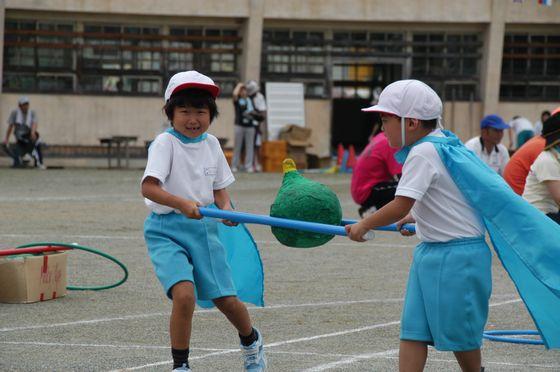 第61回宮宿小学校かぼちゃ運動会で2本の青い棒を持ち合ってかぼちゃに見立てたボールを運ぶ競技中の2人の児童の写真