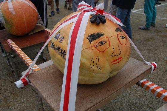 赤い眼鏡をかけた男性の似顔絵と新生宮宿小学校の文字が描かれた大きなかぼちゃが載せられた神輿の写真