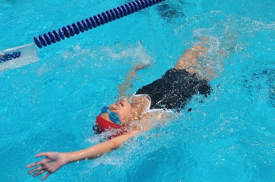 赤い水泳帽をかぶった一人の選手が背泳ぎで精一杯泳いでいる様子の写真