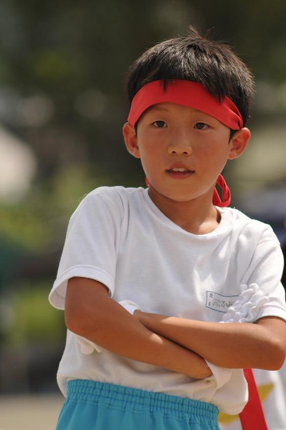 応援合戦で腕を組んでいる赤いハチマキをした男児生徒の写真