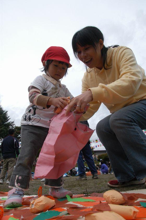 さゆり保育園の園庭で母親が持つピンク色のエコバッグに紙でできた食べ物を入れる園児の写真