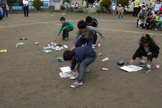 競技「森をきれいにしよう」で園庭に落ちているゴミを拾う地元の小学生たちの写真