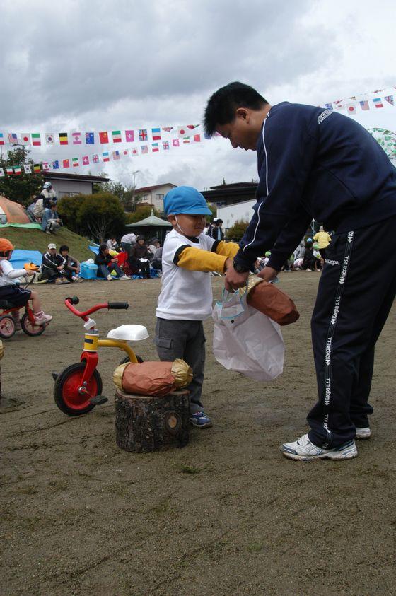 「親子競技 地球にやさしいお買い物」で購入した大きな木の実を父親の持つ白いエコバッグに入れる男の子の園児の写真