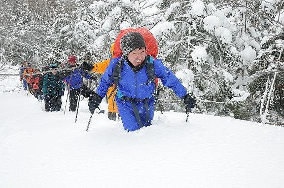膝まで雪に浸かりながらトレッキングする参加者の写真